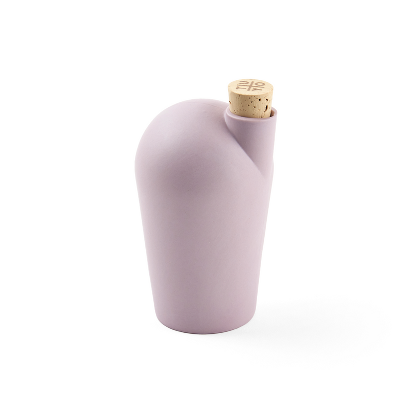 A hand holding a lavender colored carafe with a cork stopper.