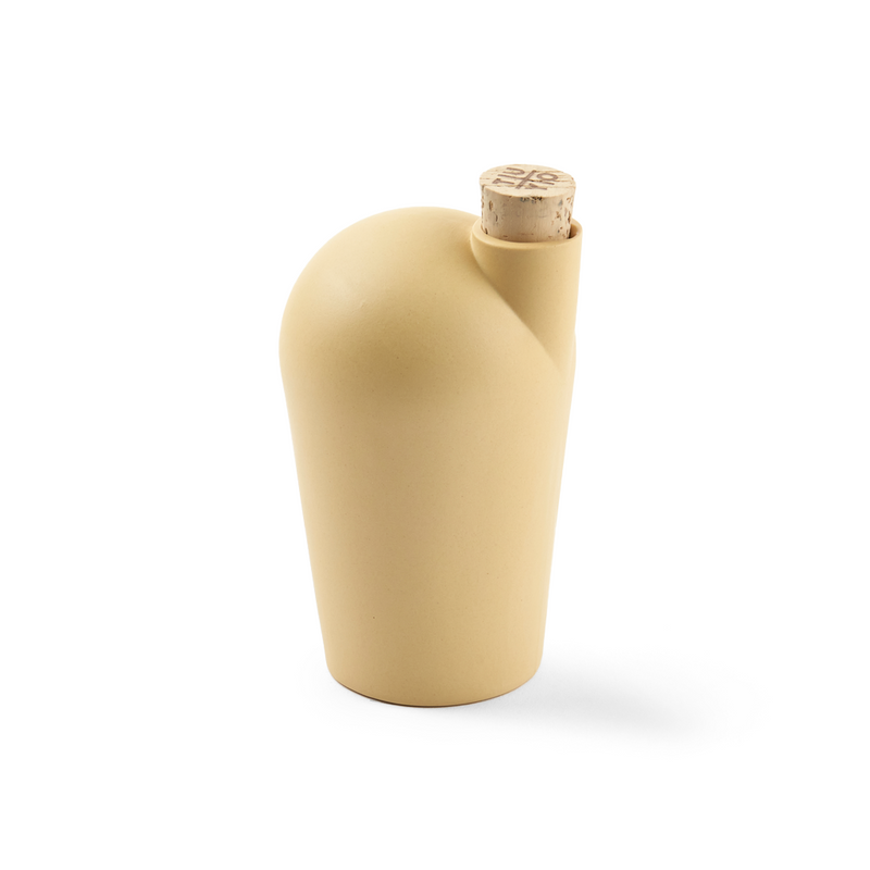 A hand holding a yellow carafe with a cork stopper.