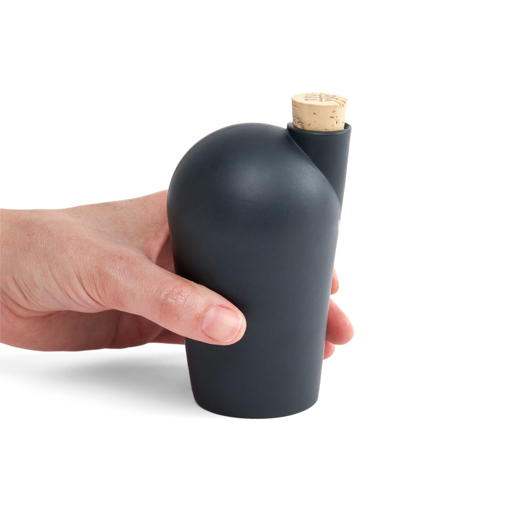 A hand holding a black carafe with a cork stopper.