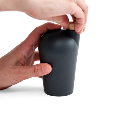 Two hands holding a black carafe uncorking the top.