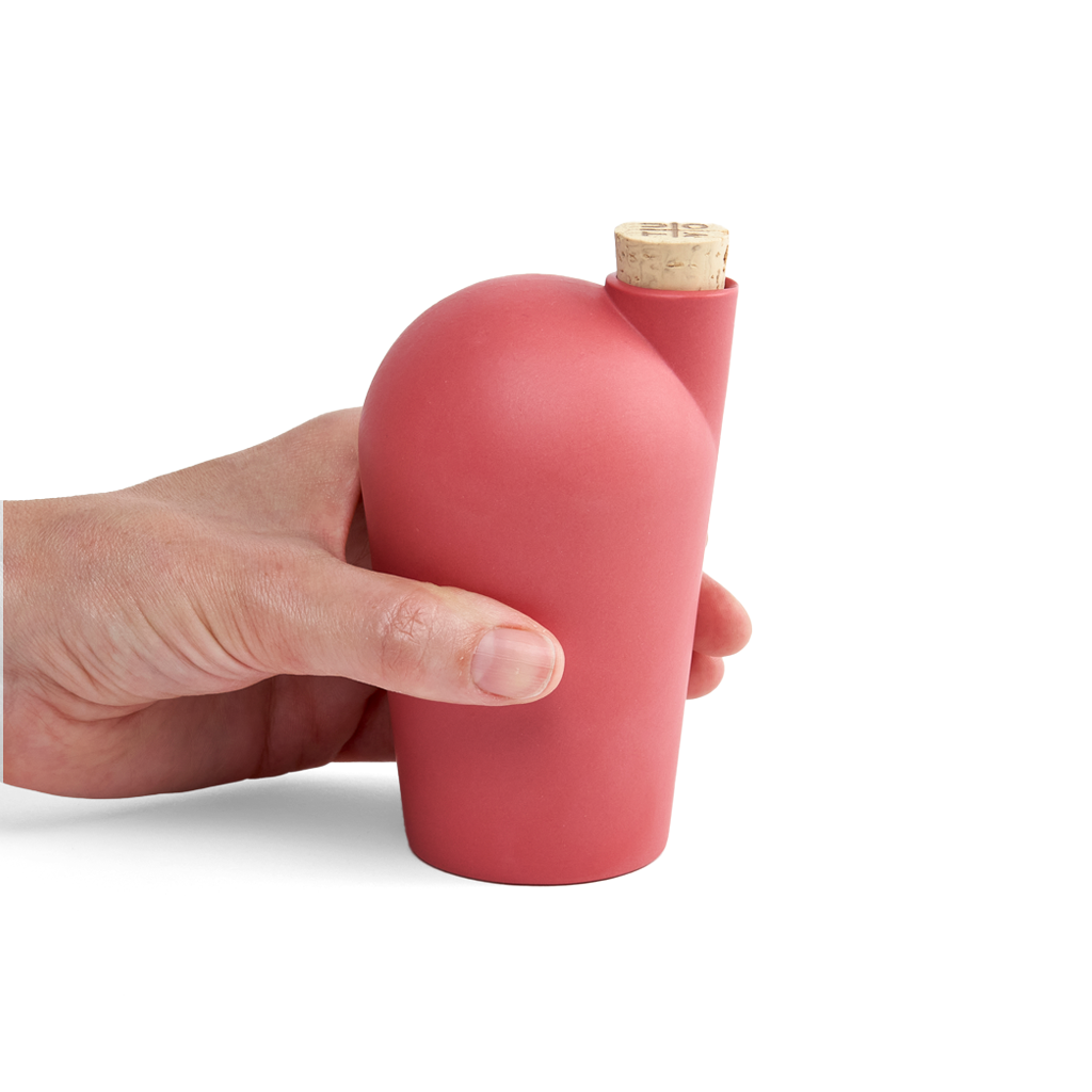 A hand holding a red carafe with a cork stopper.