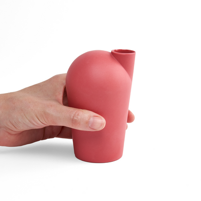 A side view of a hand holding a porcelain red carafe.