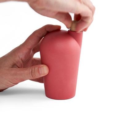 Two hands holding a red carafe uncorking the top.