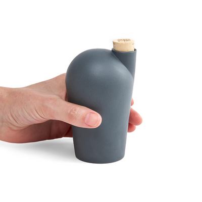 A hand holding a dark grey carafe with a cork stopper.