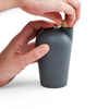 Two hands holding a gray carafe uncorking the top.