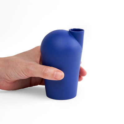 A side view of a hand holding a porcelain dark blue-colored carafe.