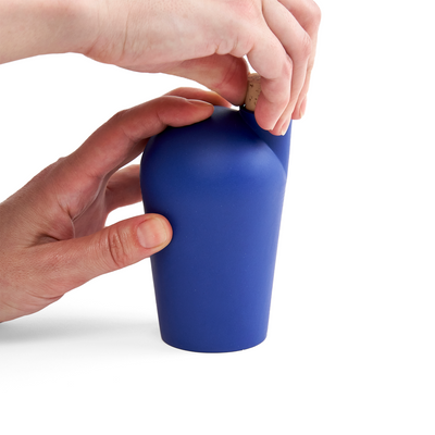 Two hands holding a dark blue carafe uncorking the top.