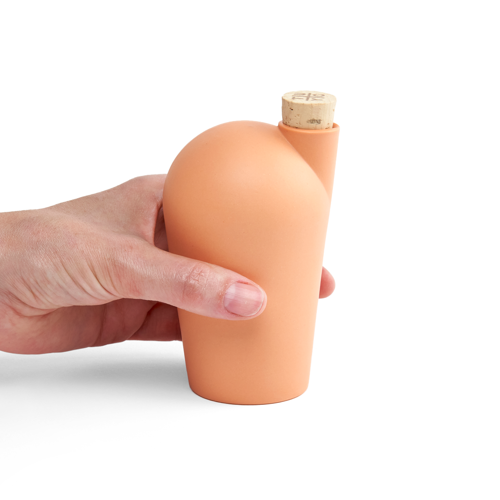 A hand holding an orange carafe with a cork stopper.