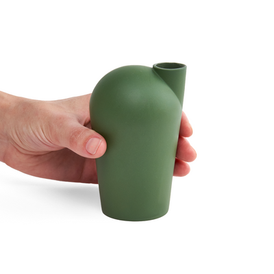 A side view of a hand holding a porcelain green carafe.
