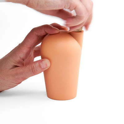 Two hands holding an orange carafe uncorking the top.