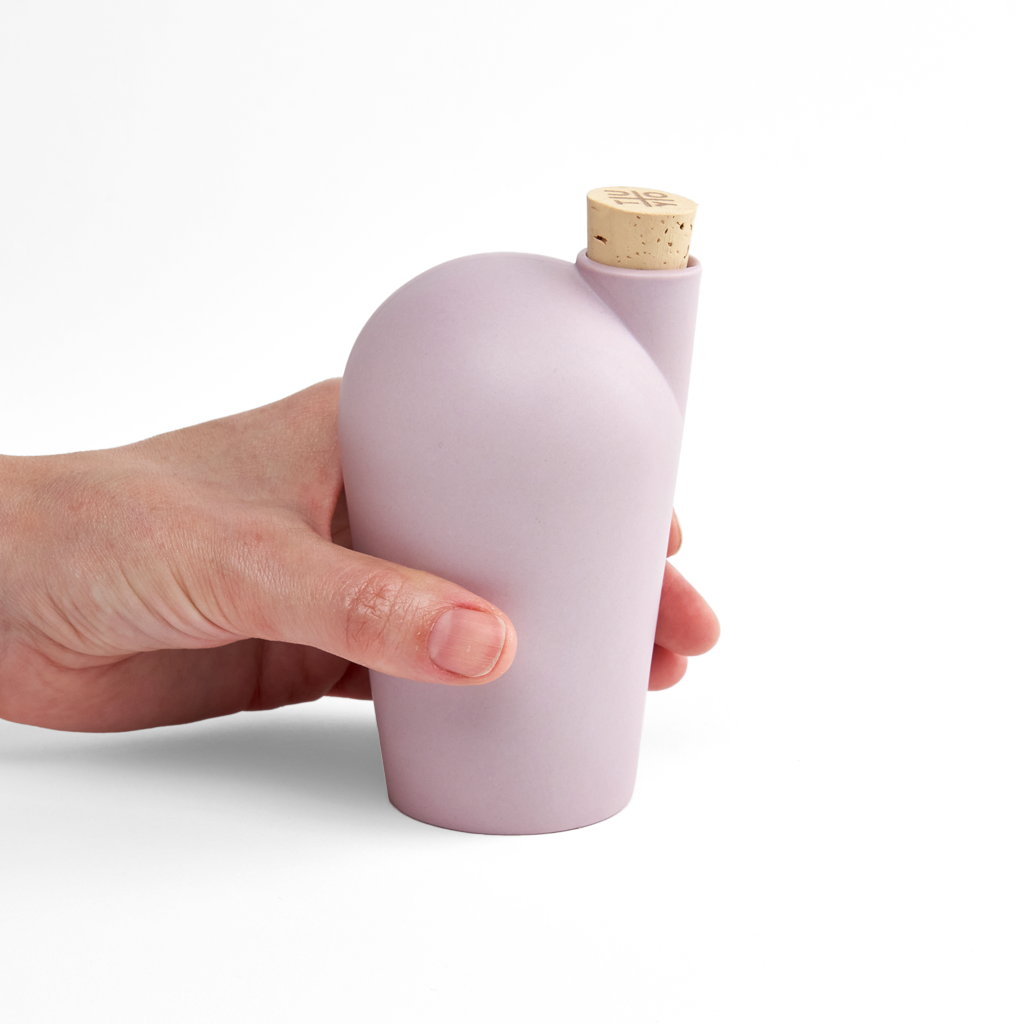 A hand holding a lavender colored carafe with a cork stopper.