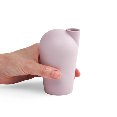 A side view of a hand holding a porcelain light purple carafe.