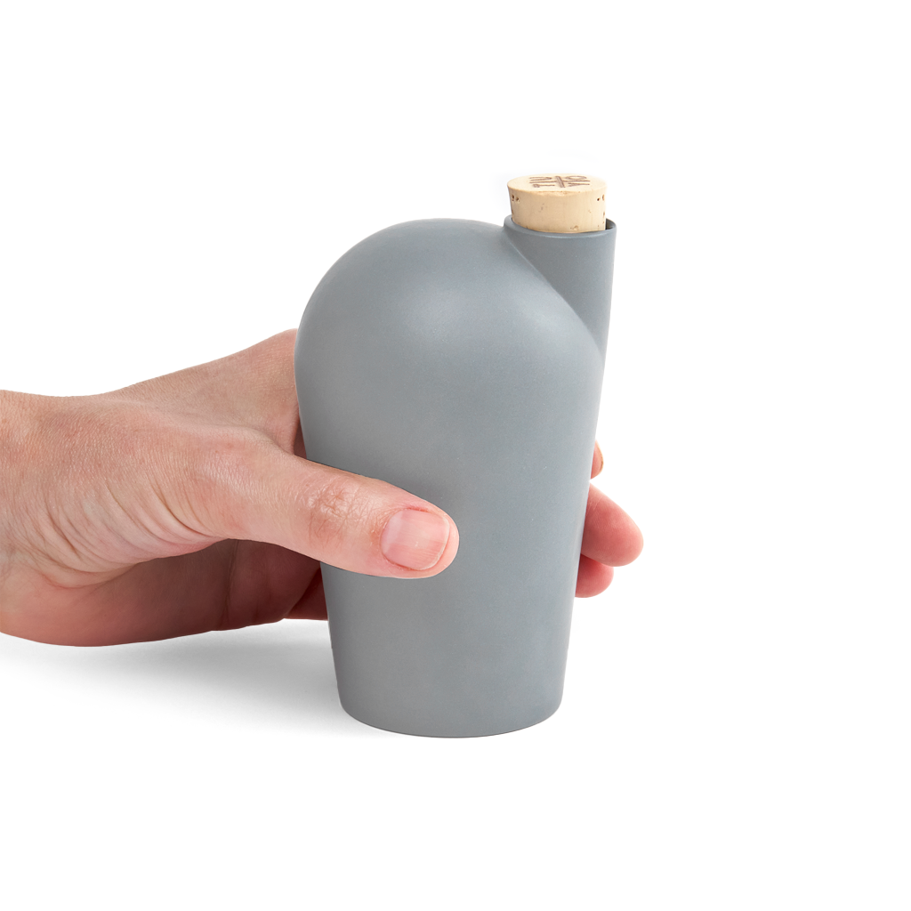A hand holding a light grey colored carafe with a cork stopper.