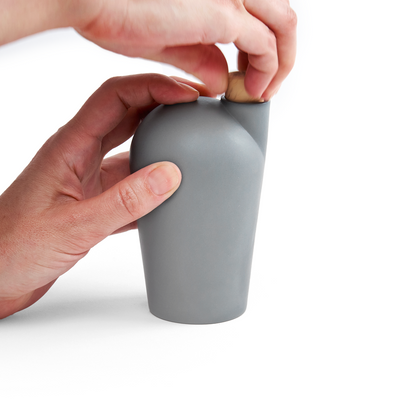 Two hands holding a light grey carafe uncorking the top.