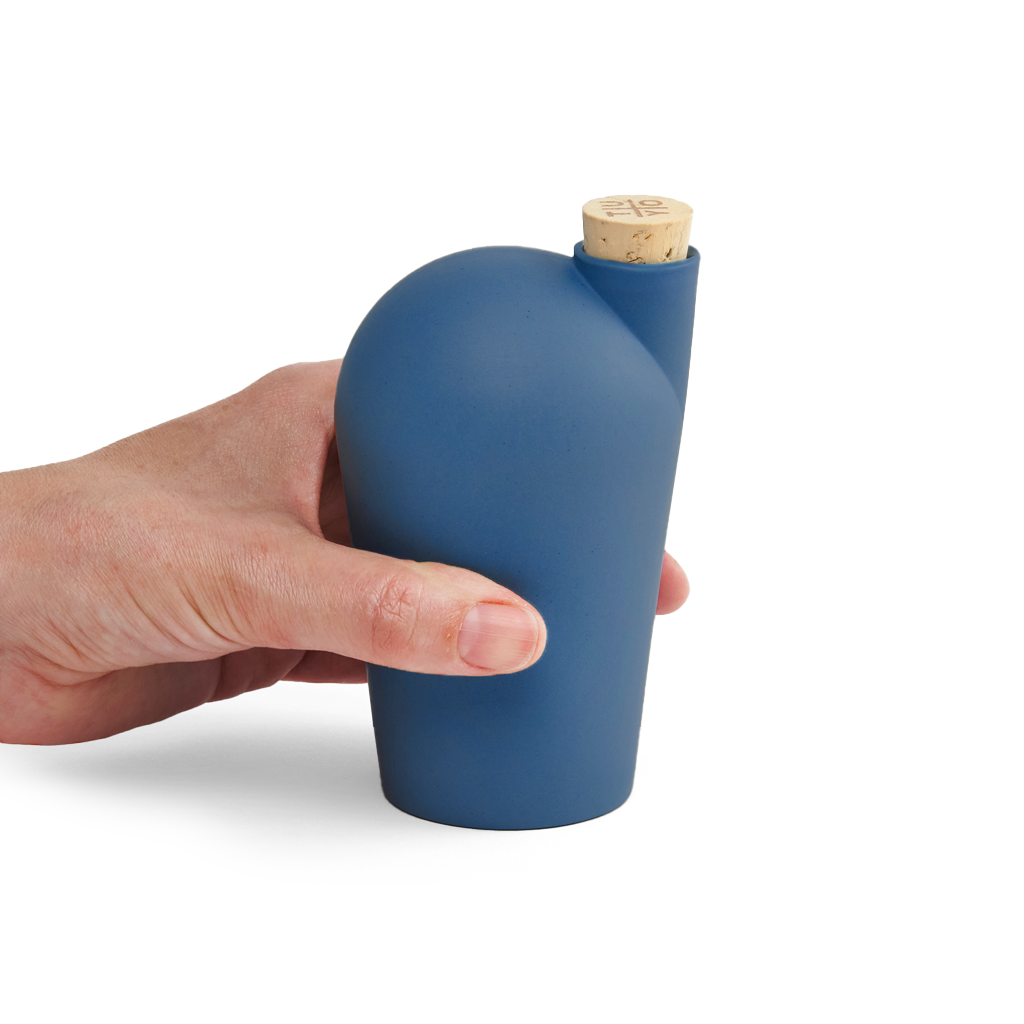 A hand holding a dark sea green carafe with a cork stopper.
