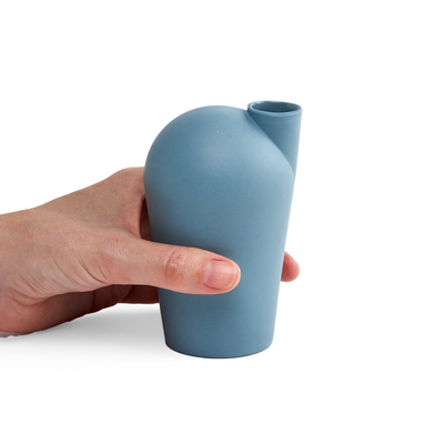 A side view of a hand holding a porcelain light teal carafe.