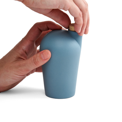 Two hands holding a turquoise carafe uncorking the top.