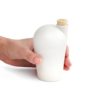 A hand holding a white carafe with a cork stopper.