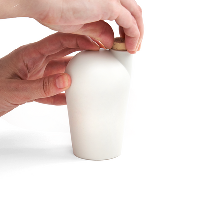 Two hands holding a white carafe uncorking the top.