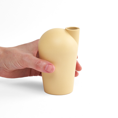 A side view of a hand holding a porcelain yellow carafe.