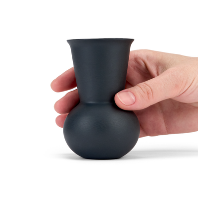 A hand holding a  black charcoal colored tequila sipping glass